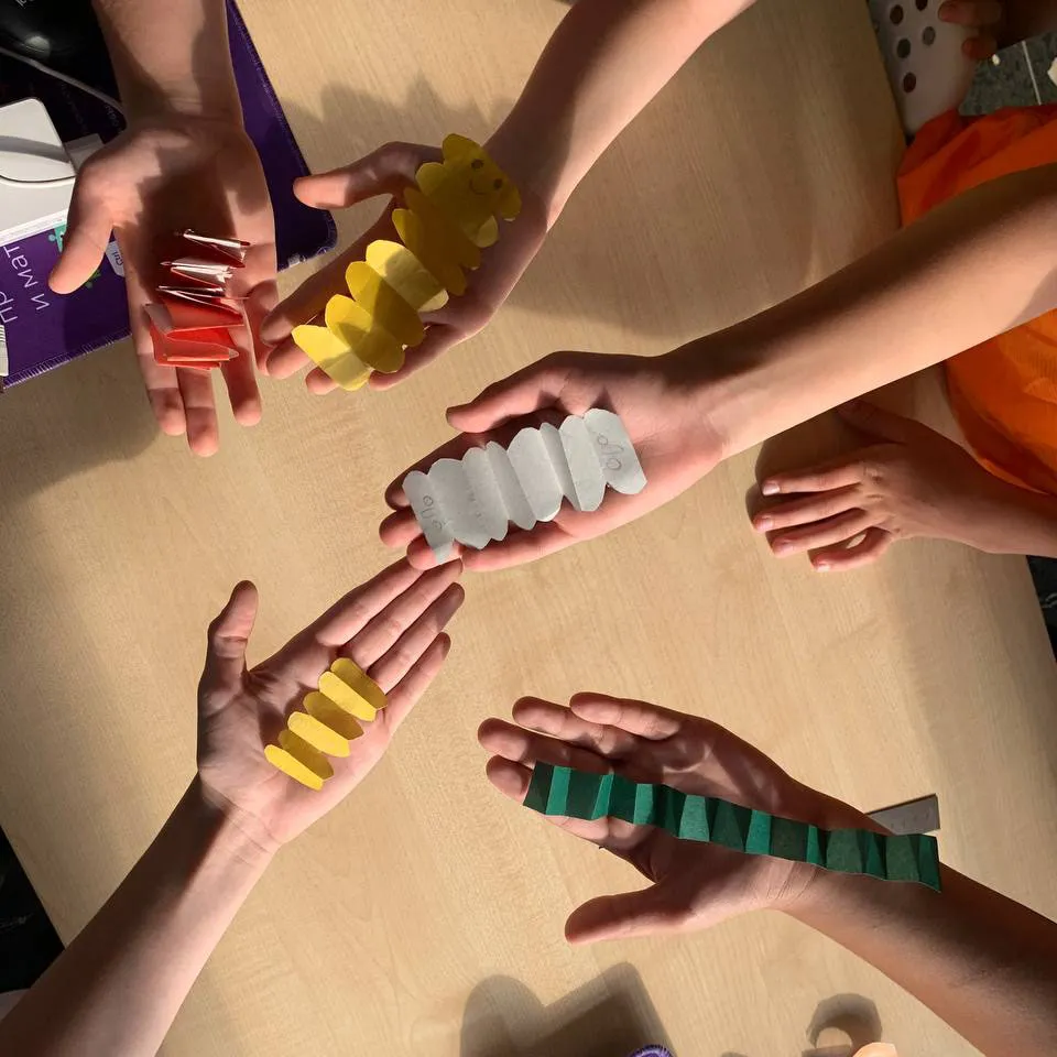 Детские руки держат бумажные «гусеницы»-гармошки разных цветов на столе — мини-проект на занятии Лиги Роботов, Екатеринбург