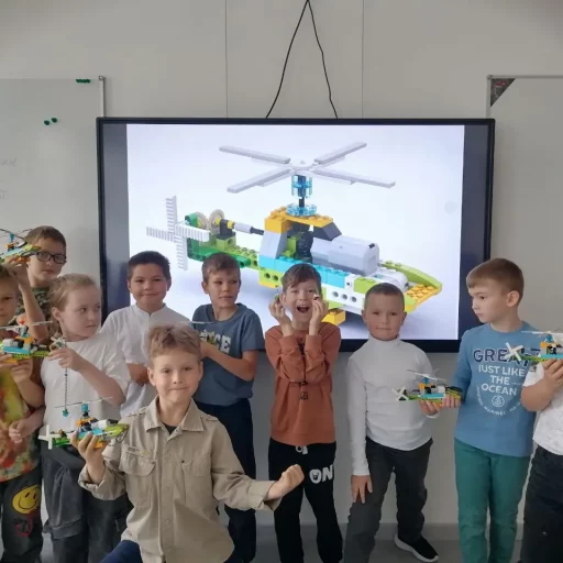Группа детей 7–10 лет с собранными вертолётами из LEGO Education на уроке в Лиге Роботов, Екатеринбург; на экране — модель вертолёта